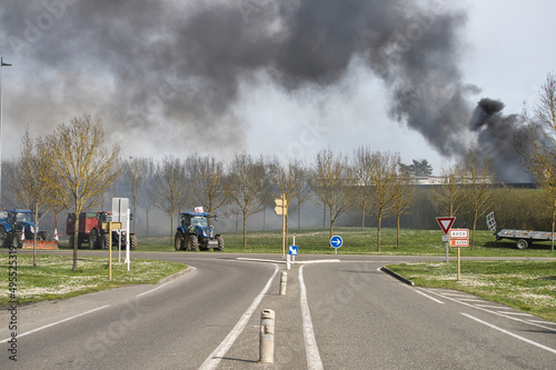 Two-way road, leading to a roundabout on which sits a tractors surrounded by black smoke. Agricultural event