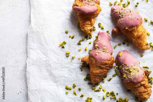 Mini-croissants with ruby chocolate and pistachios on a baking paper, gray background. Top view and copy space.