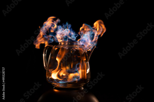 Fire within a see through glass tea pot showing beautiful orange and blue flames inferno giving the idea of substance or alcohol abuse.