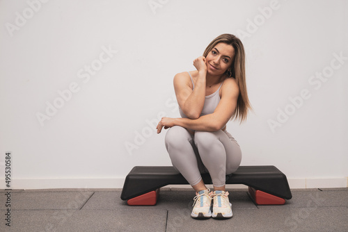 A cute adult girl sitting on a step aerobics while looking at the camera smiling.healthy life concept.