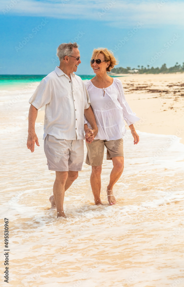 Happy senior couple walking on white sandy beach Happy senior couple walking on white sandy beach