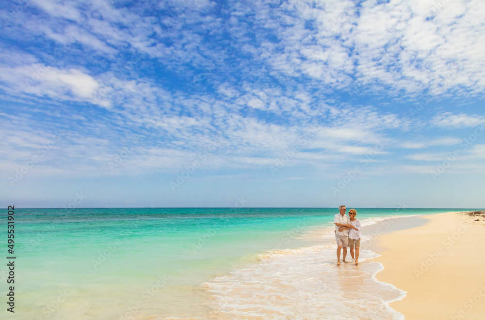 Deserted island with senior couple walking along shoreline Deserted island with senior couple walking along shoreline