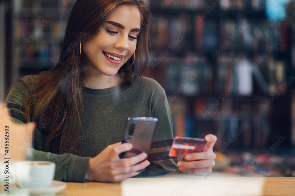 Woman using smartphone and a credit card for online shopping in a cafe Woman using smartphone and a credit card for online shopping in a cafe