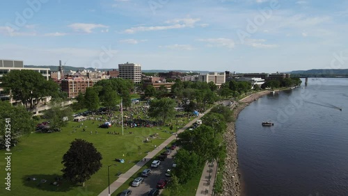 Flyover Riverside Park, La Crosse, Wisconsin, along the Mississippi River during music night in the park on a summer day. Downtown office buildings. Bluffs with forest covering. 