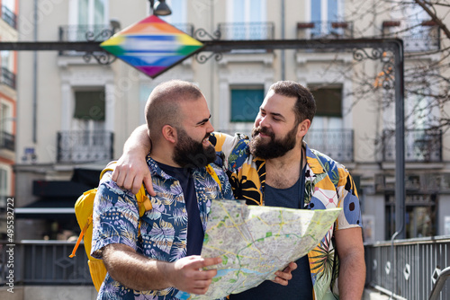 Young gay couple with tourist map at the exit of a transport station. Concept of people traveling and vacation.