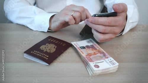 Close-ups of men's hands shopping online on the phone. Buy online cash banknotes in five thousand Russian rubles. There are Russian money and a Russian passport on the table.