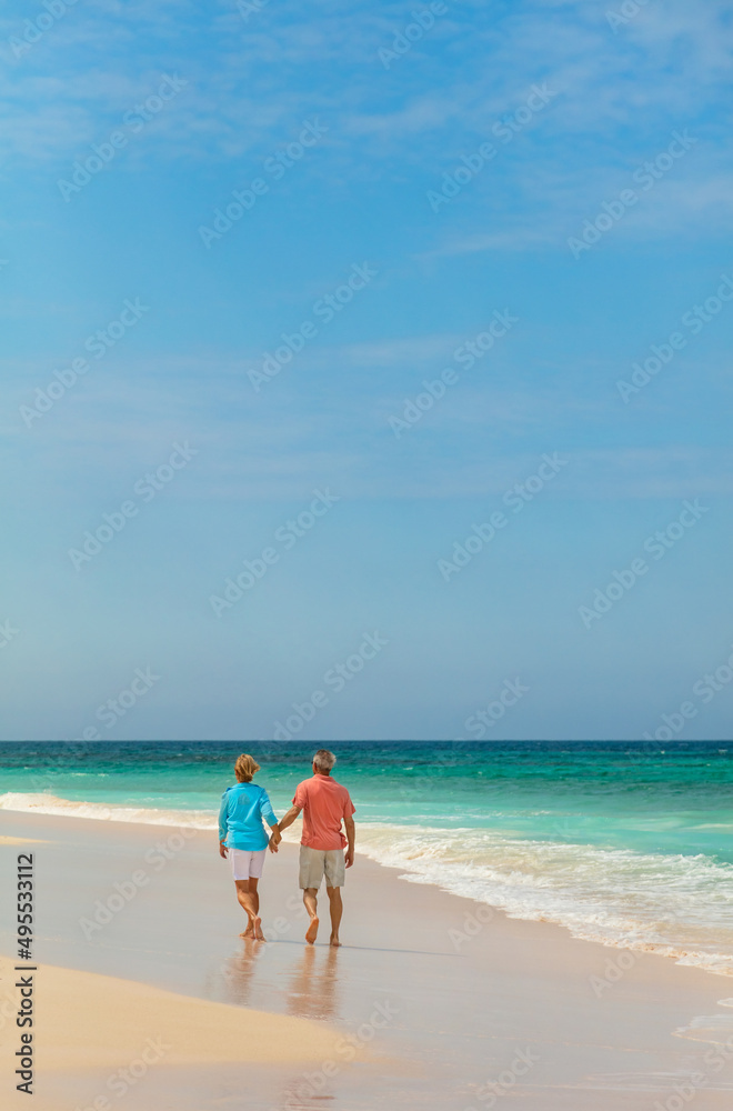 Retired Caucasian couple walking by ocean holding hands