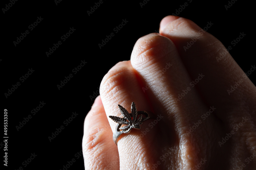 Close-up of a silver ring in the form of a marijuana leaf worn on a hand. White gold jewelry. Drug addiction symbol. Illegal distribution of harmful substances. Sign. Banner. Copy space. Dealer sign