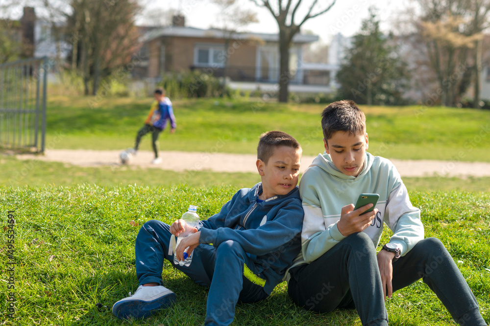 Children spend time together in nature. They play games on their phones, drink bottled water, play football. Happy childhood concept Children spend time together in nature. They play games on their phones, drink bottled water, play football. Happy childhood concept