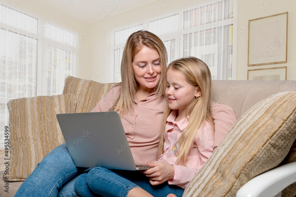 Young mom and daughter spend time together at home. They are sit on the couch with a laptop Young mom and daughter spend time together at home. They are sit on the couch with a laptop