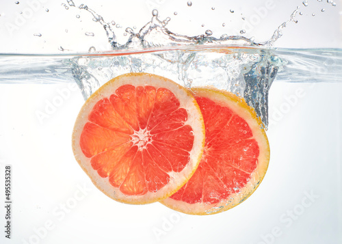 Two slices of fresh red grapefruit being splashed into water. Beautiful juicy piece of citrus grapefruit taking a plunge into water. Fresh natural orange citrus flavour.
