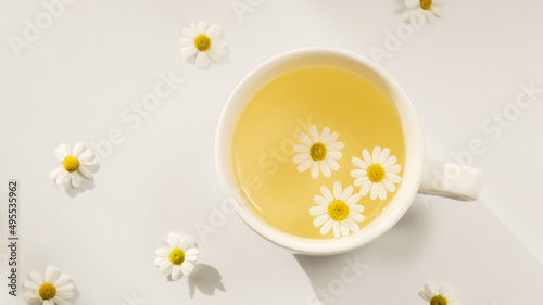 A cup of chamomile tea on a white background with flower buds inside. Soothing and healing natural herbal infusion. Flat lay, top view.