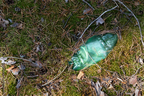 Green plastic bottle has long been lying on ground in forest. Pollution environment. Long decaying waste in nature. Disposable plastic