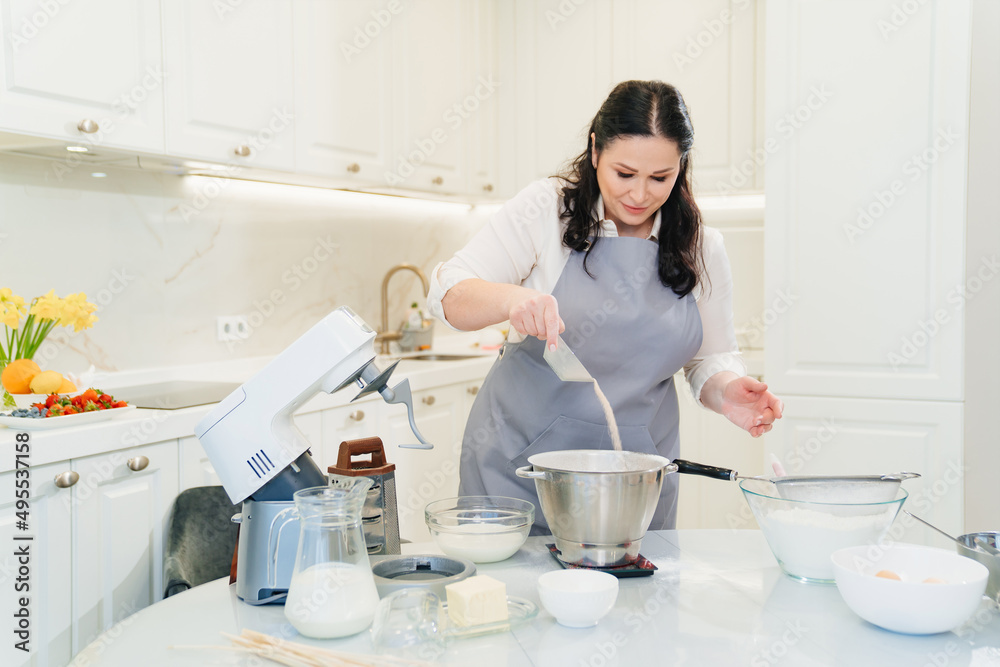 A woman cook adds a yeast to prepare dough in a mixer bowl. A woman cook adds a yeast to prepare dough in a mixer bowl.