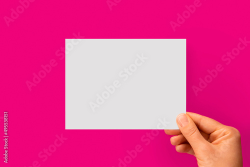 Woman's hand holding white blank paper on a pink background