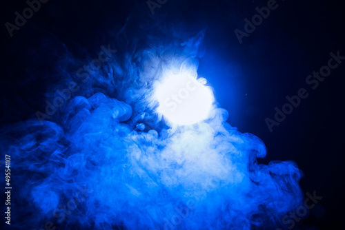 Artificial magic smoke in blue light on black background