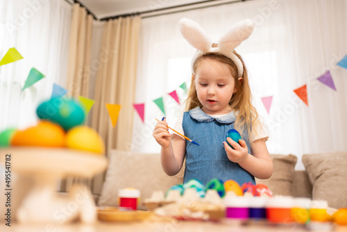 little girl with rabbit ears decorates Easter eggs with paints 