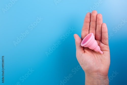Close up view of woman holding pink menstrual cup isolated over blue background, woman's period, menstrual cup in hands, modern methods for crytical days. Gynecology and hygiene products concept.