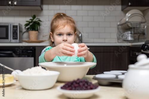 Little girl cooking in kitchen. Child sitting at table with food. Kid baking at home