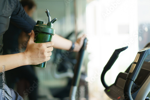 Active Asian young man making a cardio exercise on the elliptical exercise machine and drinking a water.