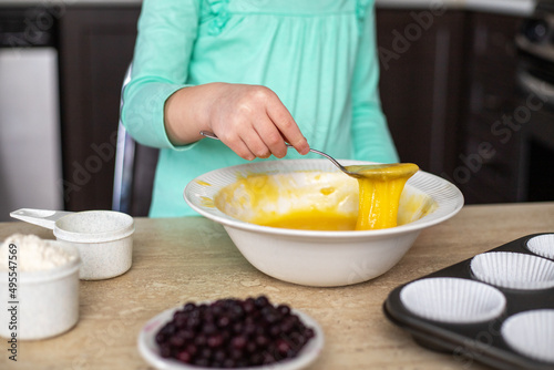 Child mixing ingredients in bowl for baking homemade muffins. Kid cooking in kitchen