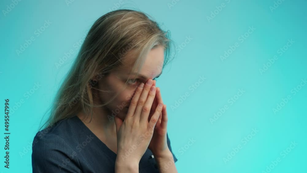 Exhausted caucasian surgeon in her 30s covering her face with two palms over blue background. Studio shot. High quality 4k footage Exhausted caucasian surgeon in her 30s covering her face with two palms over blue background. Studio shot. High quality 4k footage
