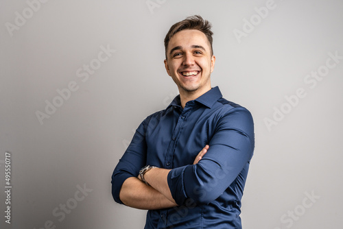 Portrait of one adult caucasian man 25 years old looking to the camera in front of white wall background smiling wearing casual blue shirt copy space