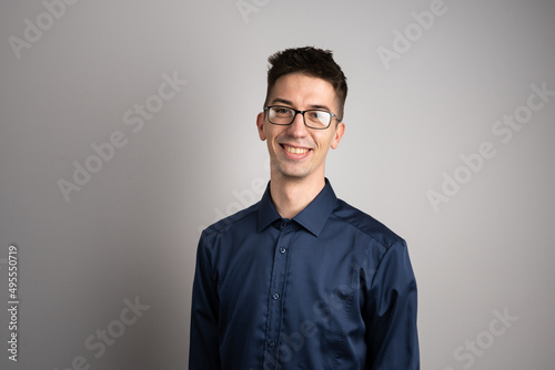 Portrait of one adult caucasian man 25 years old with eyeglasses looking to the camera in front of white wall background smiling wearing casual shirt copy space