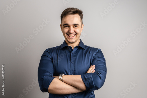 Portrait of one adult caucasian man 25 years old looking to the camera in front of white wall background smiling wearing casual blue shirt copy space