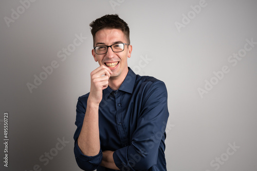 Portrait of one adult caucasian man 25 years old with eyeglasses looking to the camera in front of white wall background smiling wearing casual shirt copy space