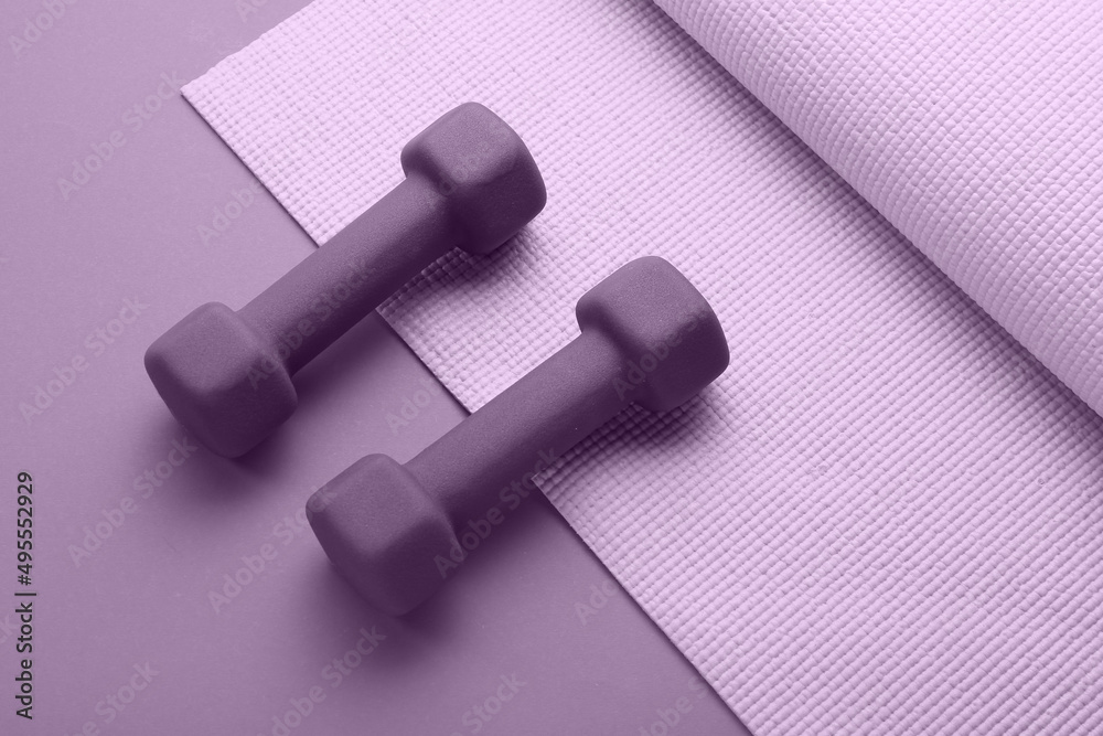 Pair of dumbbells and yoga mat on color background