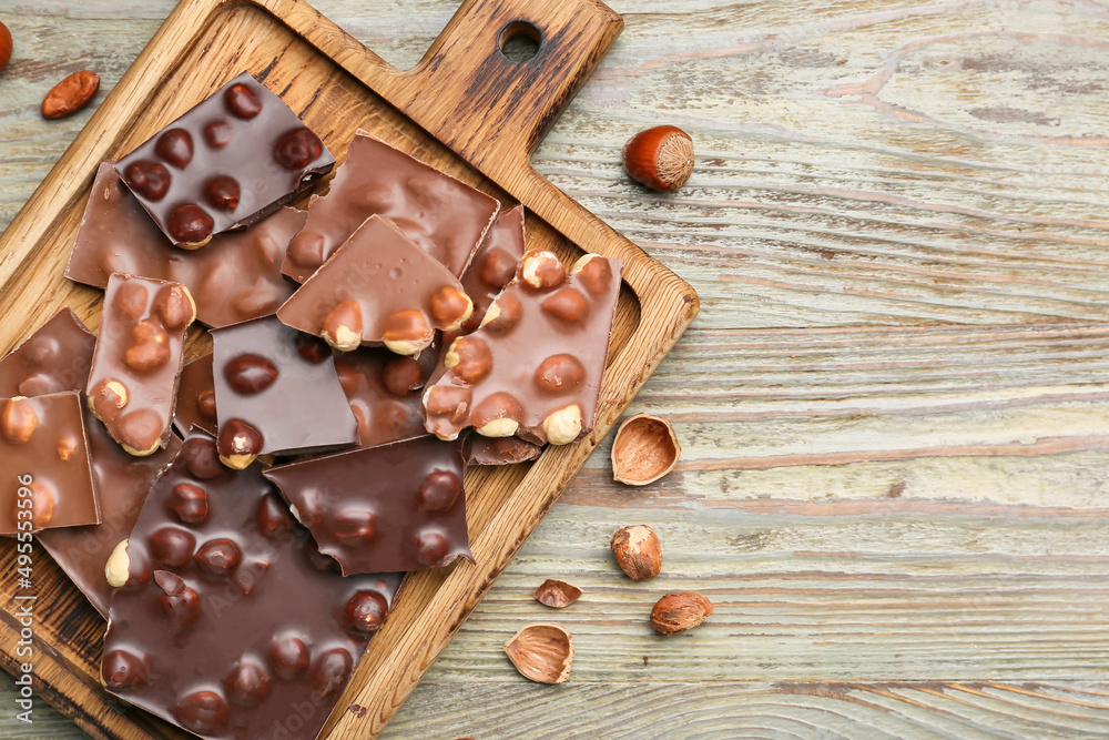 Board with pieces of tasty chocolate and hazelnuts on table