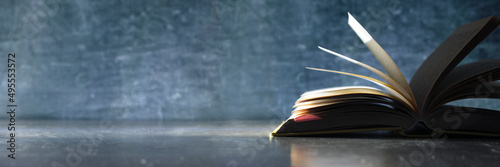 Open book, hardback book on wooden table on dark background. Home office,back to school,education,reading. Copy space,negative space technique.