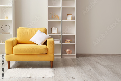 Yellow armchair with pillow and shelving units near light wall