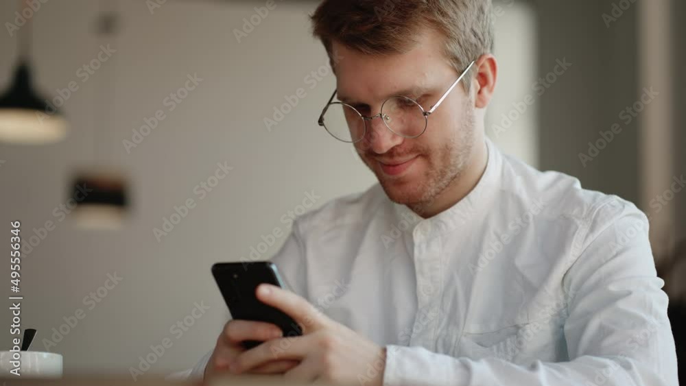 attractive man with glasses is viewing funny pictures and video in social media on smartphone display in cafe attractive man with glasses is viewing funny pictures and video in social media on smartphone display in cafe