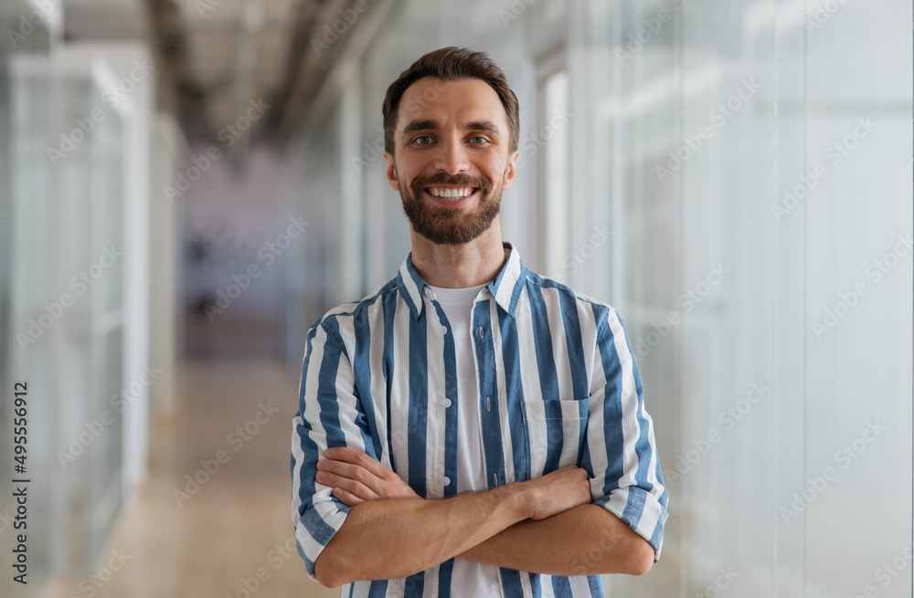 Portrait of handsome smiling businessman with arms crossed looking at camera standing in modern office Portrait of handsome smiling businessman with arms crossed looking at camera standing in modern office