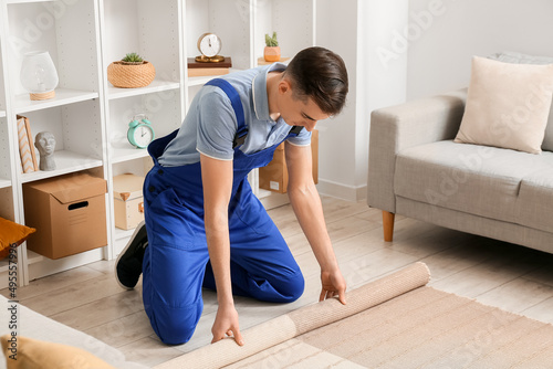 Male worker rolling stylish carpet in room