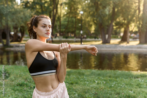 Young woman stretches her arms while doing sports in the park