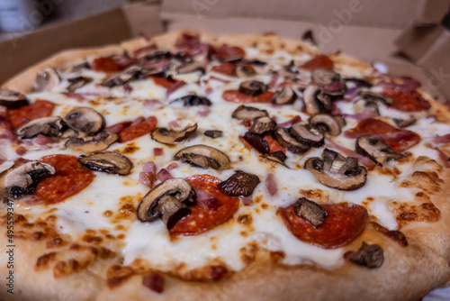 Macro, selective focus on a cheesy delivery pizza, topped with fresh mushrooms and pepperoni inside a cardboard box