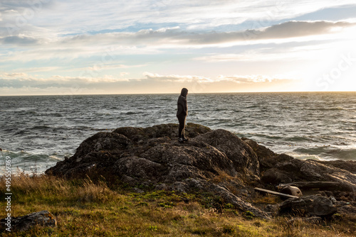 View of a silhouetted man standing the the rocky coastline on San Juan Island at sunset, with thin white clouds in the background