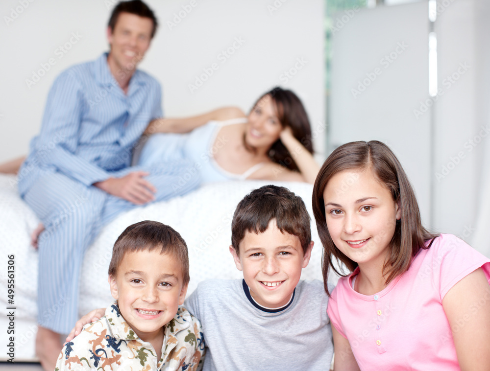 Special time with the family. Portrait of three siblings smiling as their parents sit blurred in the background. Special time with the family. Portrait of three siblings smiling as their parents sit blurred in the background.