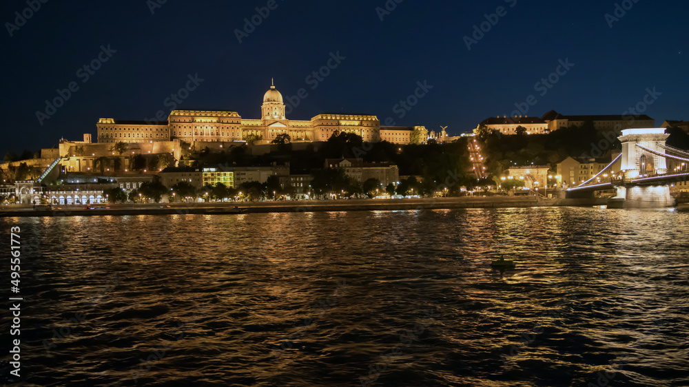 Buda Castle glows in the night overlooking the Danube River and Chain Bridge in Budapest, Hungary.
