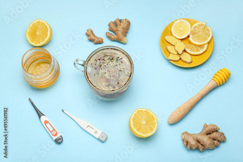 Cup of tea for sore throat, lemon slices, ginger, honey and thermometers on blue background