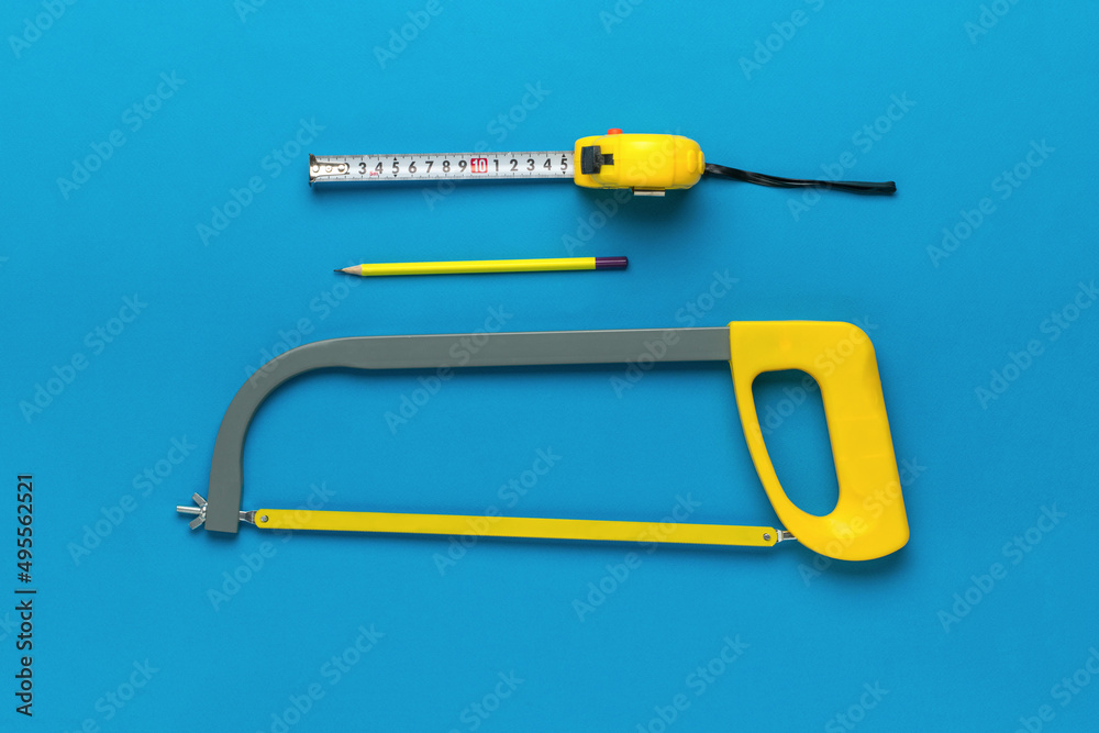 Metal hacksaw, pencil and measuring tape on a blue background. A set of tools. Flat lay.