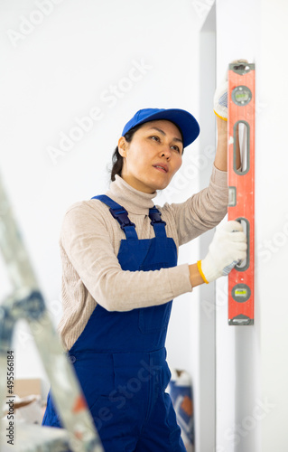 Woman builder using building level measures the vertical of a wall