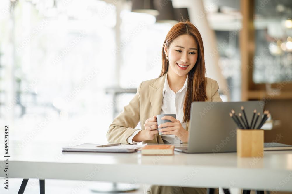 Beautiful young smiling Asian businesswoman working on laptop and drinking coffee, Asia businesswoman working document finance and calculator in her office. 