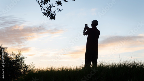 Silhouette of a man taking photos using mobile phone on a hilltop at dawn © Janice