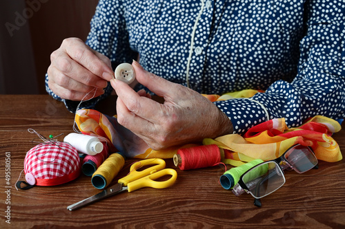 hands of an elderly woman with sewing needle and button. Tailor's hands at work close-up. Employment of  elderly