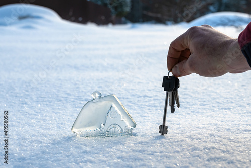 beautiful miniature glass, crystal house and man's hand with keys on background of white snow. Concept of dream house. Copy space