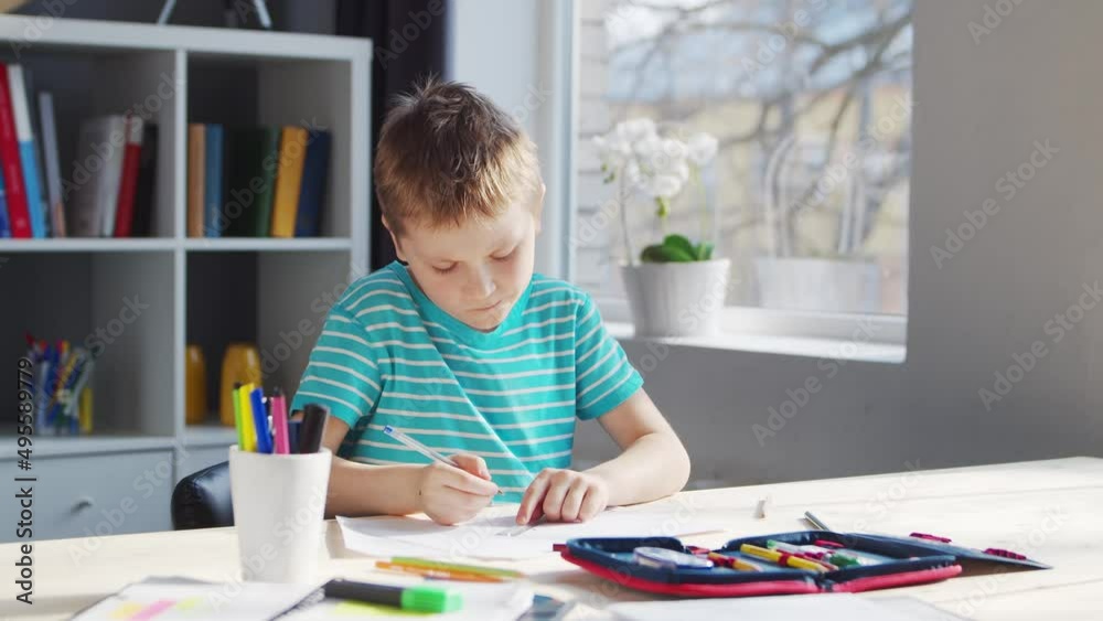 Boy is Doing his Homework at the Table. Cute Child is Learning at Home with the Help of Textbooks and School Materials. Study and Education Concept. Boy is Doing his Homework at the Table. Cute Child is Learning at Home with the Help of Textbooks and School Materials. Study and Education Concept.